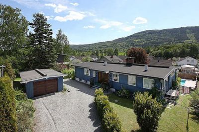 Fotografi av en blå enebolig med garasje, sett fra luft eller høy vinkel.