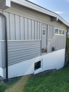 Fotografi av fasaden på en eksisterende bygning med grå panelvegger og hvit fundamentmur.