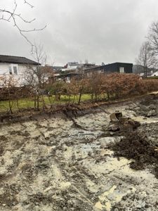 Fotografi av en byggeplass eller tomt med grus, jord og en del av en bygning i bakgrunnen.