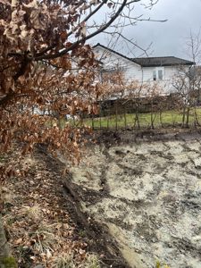 Fotografi av en hvit villa sett fra bakken, med en steinmur og trær i forgrunnen.