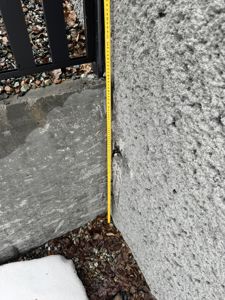 Fotografi av en vinkel i en bygning, der en gul målebånd er plassert langs en betongvegg for å måle høyde.