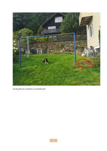 Fotografi av en bakgård med et bustadhus i bakgrunnen. Bildet viser en synlig fjellblokk (markert med rød sirkel) på vestsiden av huset.