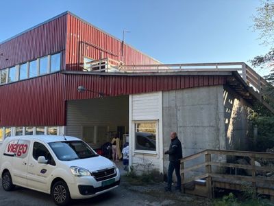 Fotografi av en eksisterende bygning med rød fasade, betongfundament og en hvit varebil foran.