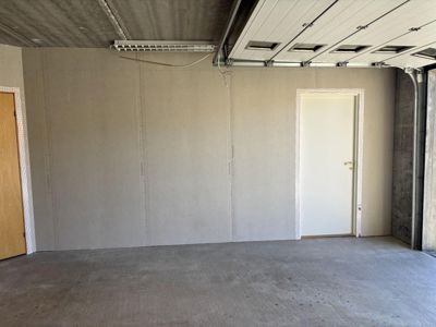Fotografi av en tom garasje eller kjeller med betonggulv, gipsvegger og en hvit garasjedør som er hevet opp.