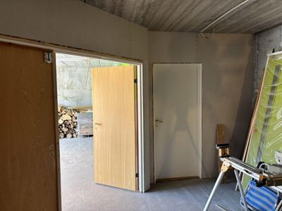 Fotografi av et rom under oppussing eller ombygging, med synlige dører, gipsvegger og utstyr.