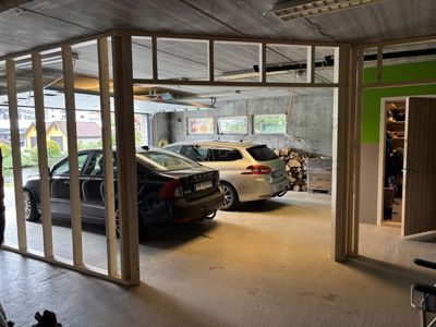 Fotografi av en garasje eller underetasje under bygging, med to biler parkert og en delvis oppført trekonstruksjon i forgrunnen.