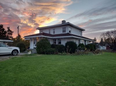 Fotografi av en hvit villa med etasjer, sett fra hagen mot en solnedgang.