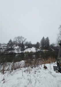 Fotografi av et snødekt landskap med en elv og hus i bakgrunnen.