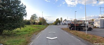 Satellittbilde eller flyfoto fra Google Earth som viser en vei, grøntområder og bygninger i et industriområde.