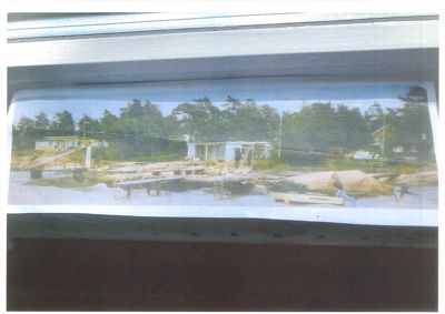 Fotografi av en bygning ved vannet med en brygge, sett gjennom et vindu.