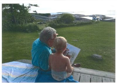 Fotografi av en mann og et barn som sitter på en terrasse og leser en tegning eller avis.