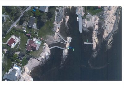 Flyfoto eller satellittbilde som viser et kystområde med hus, brygger og vann. Bildet fungerer som en situasjonsplan eller kart.