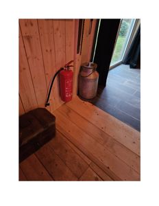 Fotografi av en innendørs scene med trepanelvegger, gulv, en brannslukker og en melkekanne.