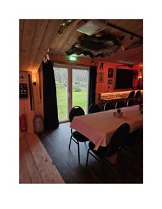 Fotografi av et interiør, sannsynligvis et spisestue- eller møterom med bord, stoler og en dør ut til hagen.