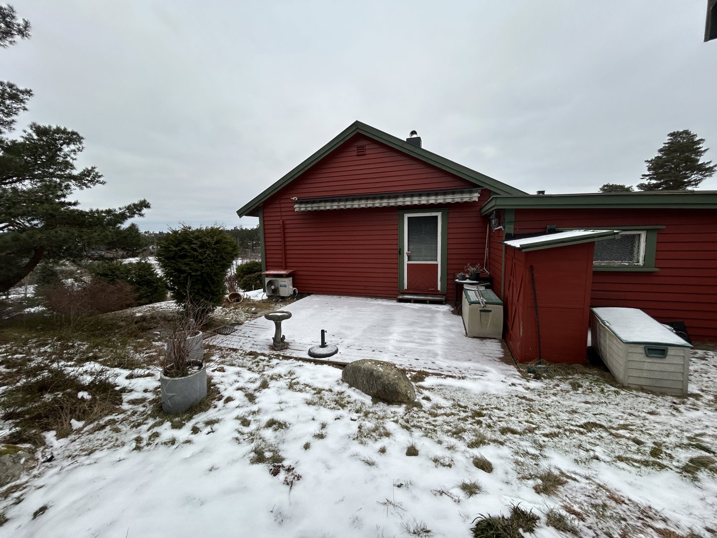 Fotografi av en rød enebolig sett fra bakgården eller siden, med snø på bakken og en liten veranda.