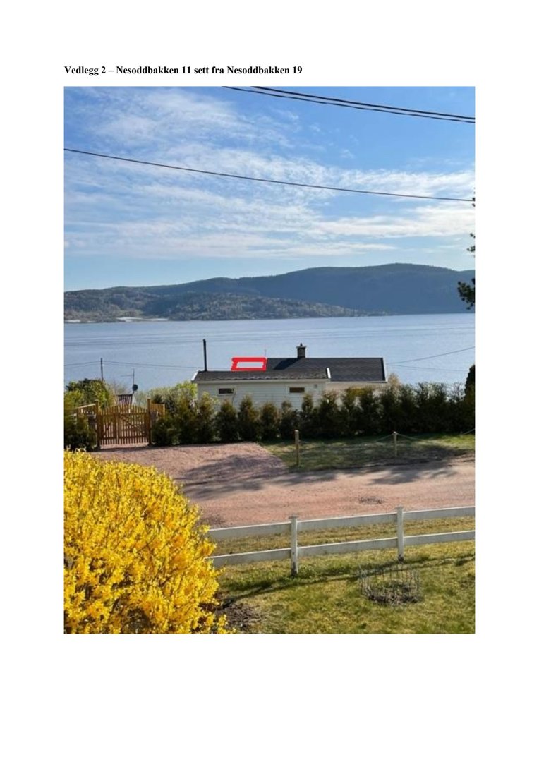 Fotografi av en bygning (Nesoddbakken 11) sett fra Nesoddbakken 19, med utsikt over vann og fjell.