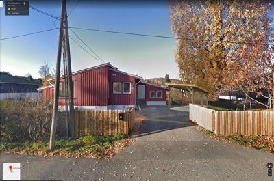 Fotografi av en rød enebolig sett fra veien, inkludert hage og kjeller.