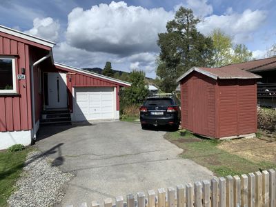 Fotografi av en rød villa med garasje, en bil og en uthus på en eiendom.