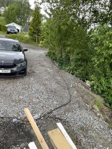 Fotografi av en grusvei eller kjørebane på et bygge- eller anleggssted, med en bil parkert på venstre side og vegetasjon på høyre side.