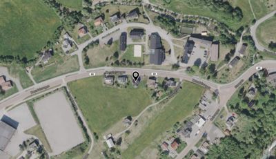 Satellittbilde (flyfoto) av et område med hus, veier og natur, med en markør som indikerer en spesifikk plassering.
