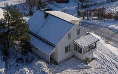 Fotografi av en hvit, toetters hus med etasjehus, sett fra luften (dronebilde) i en snødekt omgivelse.