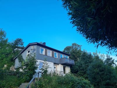 Fotografi av en toetasjes villa med grå fasade, beliggende i et skogkledt område.