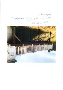 Fotografi av en utvendig terrasse eller veranda med hvite søyler og balustrader, festet til en bygning. Under terrassen er det synlig grønn hekk og en skråning.