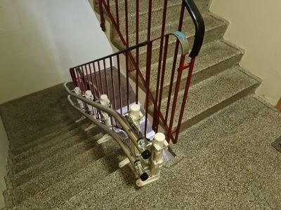 Fotografi av en trapp med en installert trappheis (stigeheis) og en rød metallhåndtak.