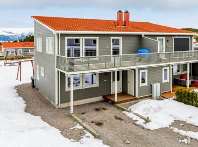 Fotografi av en ferdigbygd, toetasjes bolig med grå fasade og oransje tak, sett fra siden.