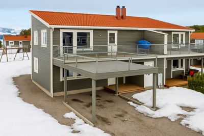 Fotografi av en ferdigbygd eller planlagt villa med grå fasade, oransje tak og utvendige trapper/balkonger, sett fra siden.