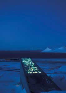 Fotografi av en lysende betongstruktur (Vårplassen) i en snødekket omgivelse ved vann.
