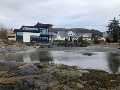 Fotografi av en moderne villa ved kysten, sett fra et lavt nivå mot vannet.