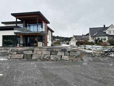 Fotografi av en moderne villa med en steinmur i forgrunnen og nabolag i bakgrunnen.