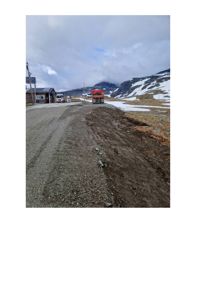 Fotografi av en vei i fjellområde med snø, fjell og en bygning i bakgrunnen.