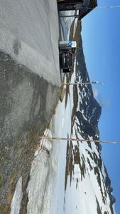 Fotografi av en vei, en bil, en del av en bygning og en snødekt fjellside.