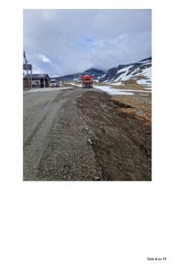 Fotografi av en vei i fjellområde med snø, fjell og en bygning i bakgrunnen.