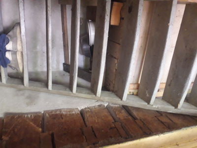 Fotografi av en eksisterende eller under oppussing bygning, som viser en trapp med tretrinn og en betong- eller steinmur med vertikale lister.