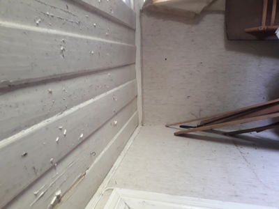 Fotografi av en innvendig hjørne i en bygning, som viser en hvitvasket panelvegg og gulv.