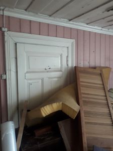 Fotografi av en hvit dør med panel i en rosa panelvegg, sett innendørs. Det er også synlig taklist og et gulv dekket av byggematerialer.