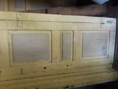 Fotografi av en gammel, gulmalt dør med paneler og metallbeslag.