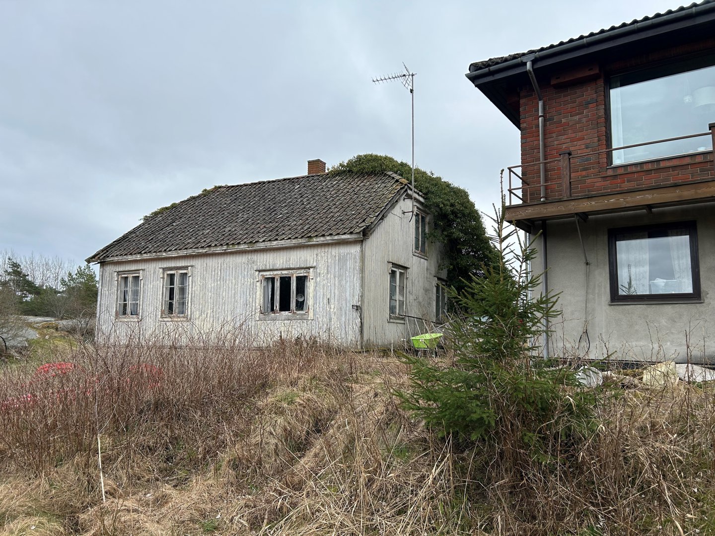 Fotografi av en gammel, hvitfarget trehytte og en del av en nyere, rødbrun bygning sett fra utsiden.