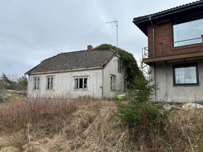 Fotografi av en gammel, hvitfarget trehytte og en del av en nyere, rødbrun bygning sett fra utsiden.