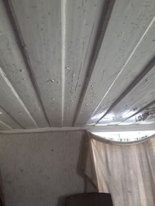 Fotografi av et tak eller en innvendig overflate med hvite, panelerte planker som viser tegn på slitasje og maling som er falt av.