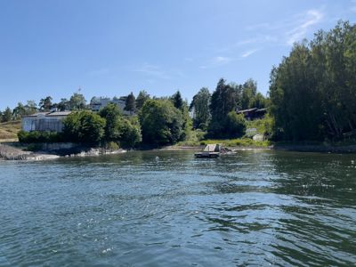 Fotografi av en bygning ved vannkanten med en brygge i forgrunnen.