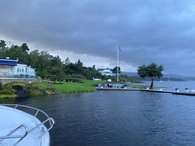 Fotografi av en bygning ved vannet med en båt i forgrunnen.