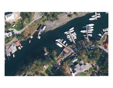 Flyfoto eller satellittbilde av et kystområde med båthavn, hus og veier.