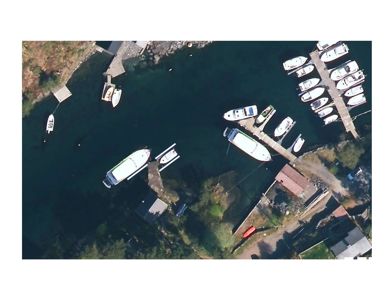 Luftfoto (satellittbilde) av en havn med båter, kai og omgivende terreng.