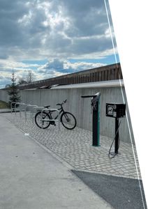 Fotografi av en utvendig scene med sykkelstøtter, en sykkel, en ladesøyler og en betongvegg foran en bygning.