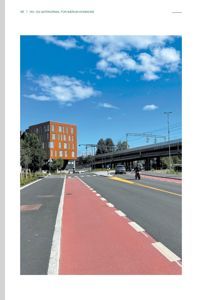 Fotografi av en gate med rød sykkelvei, en oransje bygning og en jernbanestrekning i bakgrunnen.