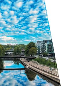 Fotografi av en bydel med en elv, broer, trær og moderne bygninger under en skyet himmel.